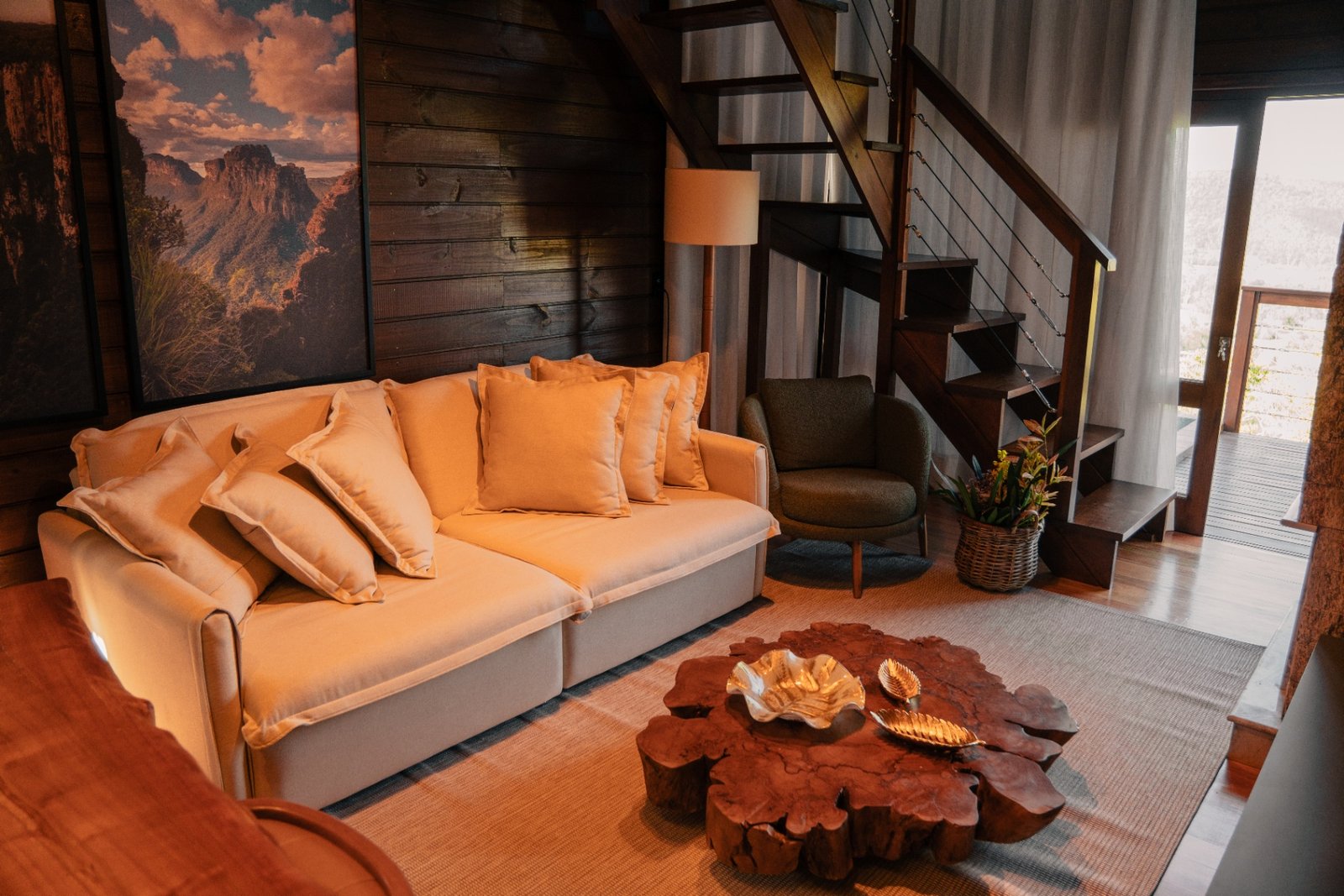 Sala de estar com sofá, mesa de centro em tronco e escada para o mezanino